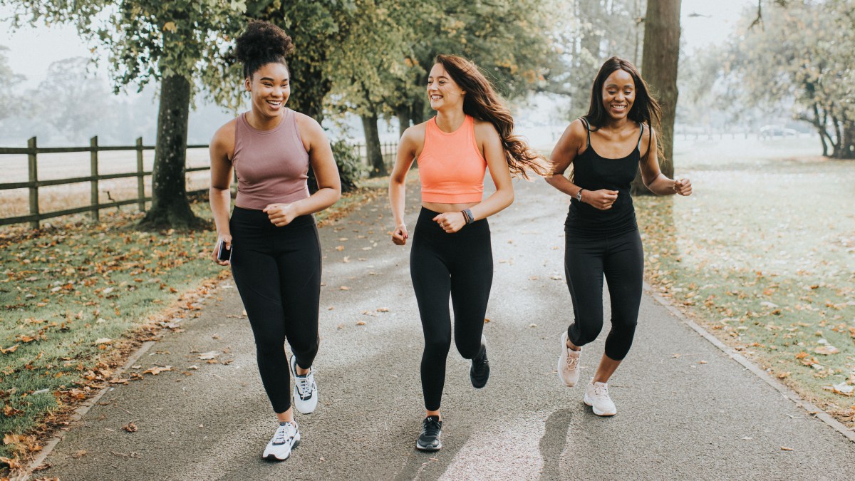 Three young women run in the park;  there are leaves on the ground and fog in the background.