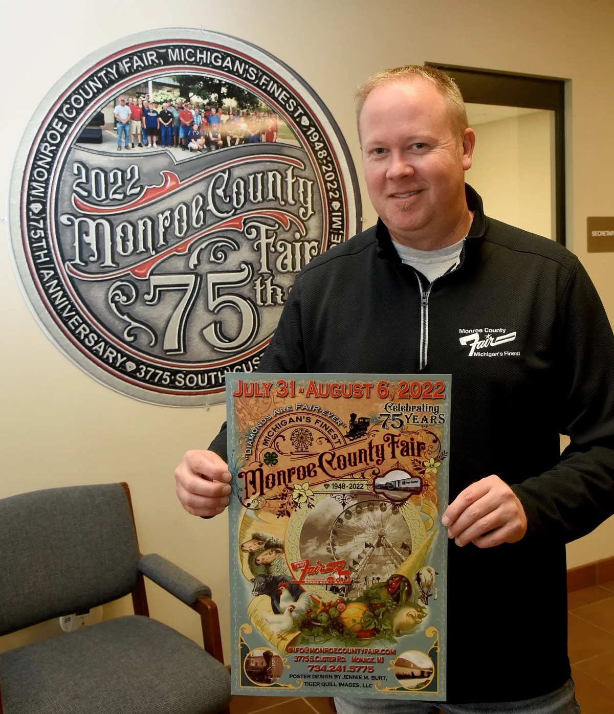 Monroe County Fair Manager Daryl Diamond holds the 75th Monroe County poster designed by Jenny Bert.  The mural is a replica of the commemorative coin for this year's fair.