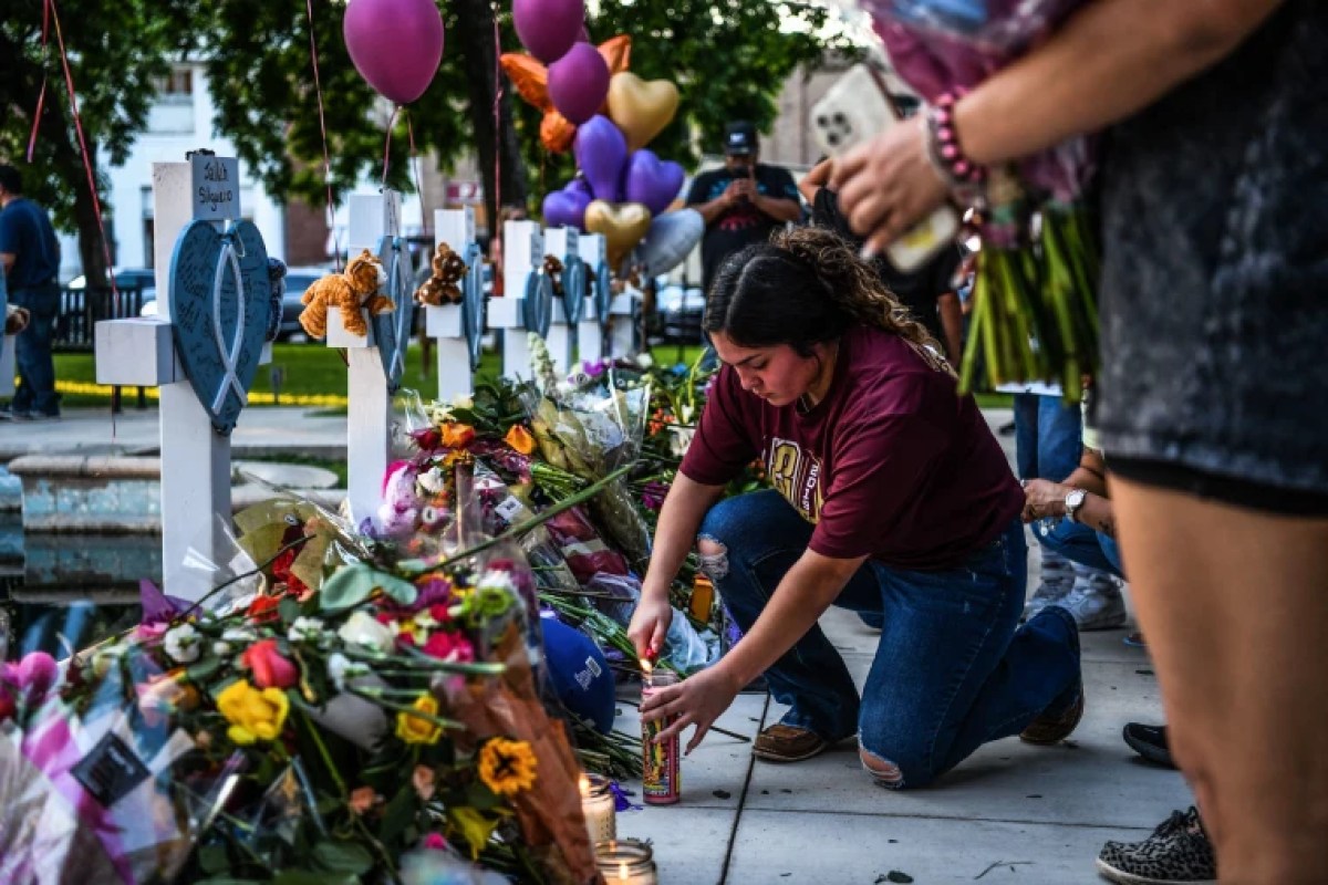 Picture: A woman lights a candle on a makeshift monument in front of the Uvalde County Courthouse in Uvalde, Texas, May 26, 2022.