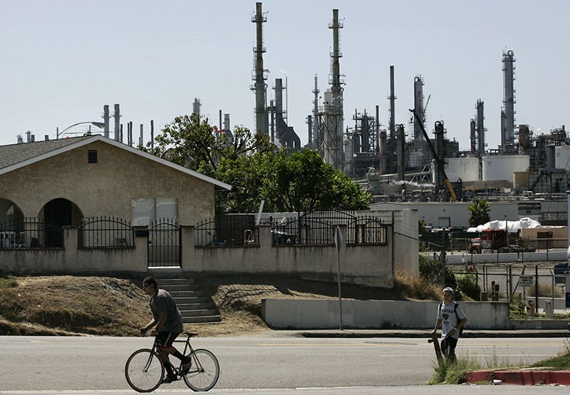 A person on a bicycle and a person on a skateboard in front of the ConocoPhillips house and refinery in Los Angeles, California, USA.